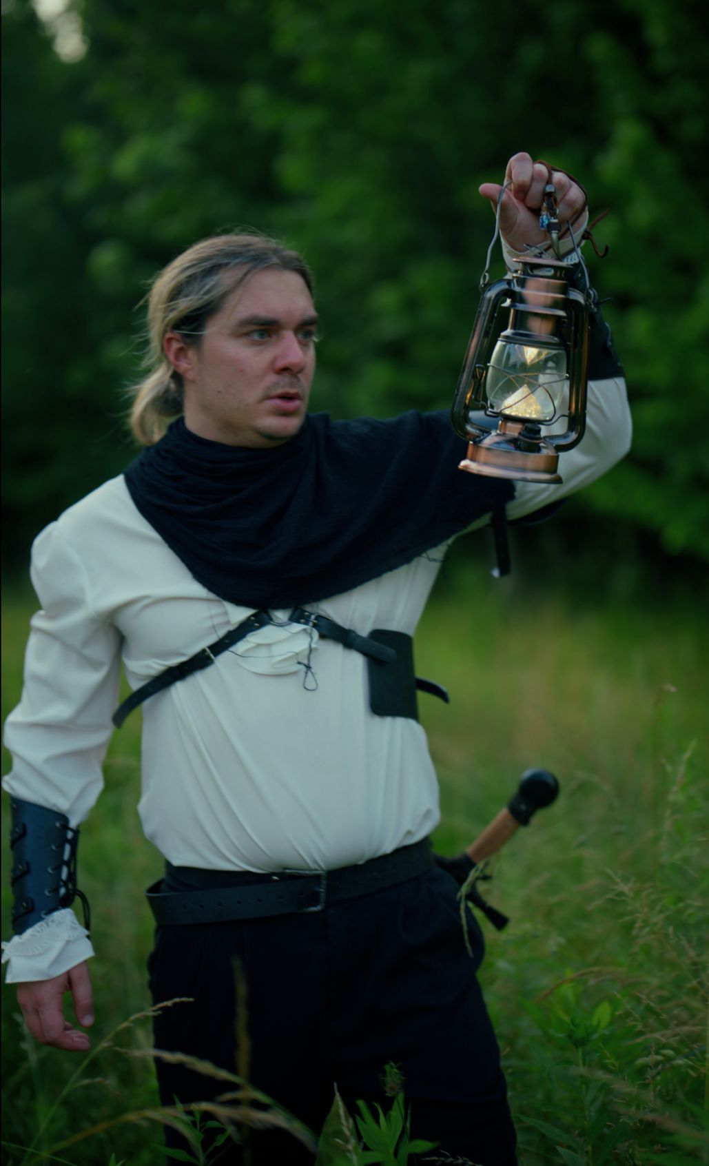 Jay Putty in costume holding a lantern in a summer field